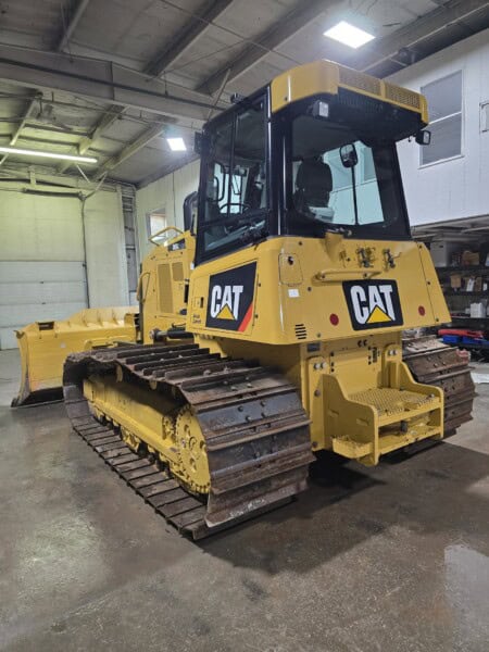 Caterpillar D6K2 bulldozer with enclosed cab, yellow body, and tracked undercarriage, parked inside a warehouse.