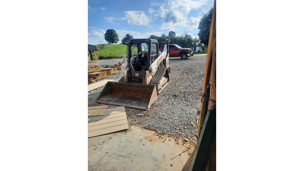 Excavator with a front bucket attachment parked outdoors on a gravel surface in a rural setting.