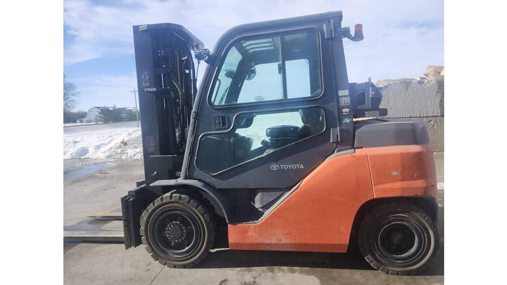 Toyota forklift, orange and black, side view, outdoor setting with snow and clear sky.