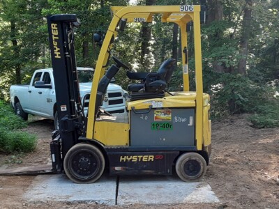 Yellow Hyster E50XM forklift with black mast and tires, parked on dirt near trees and a blue shipping container.