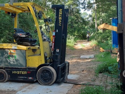 Yellow Hyster E50XM forklift with black mast and tires, parked outdoors on dirt with trees in background.