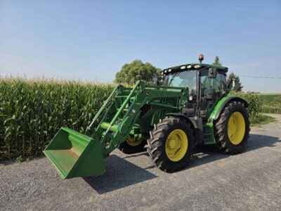 Green John Deere tractor with front loader attachment on a gravel road near a cornfield.