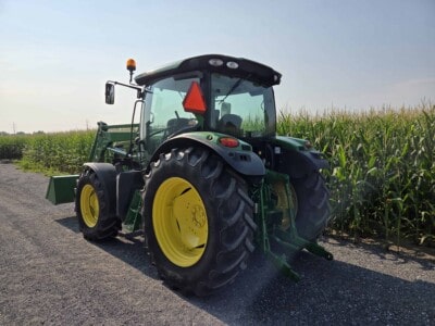 John Deere 6125R tractor with cab and large rear tires in a field of corn.