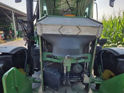 Green John Deere tractor with front loader and enclosed cab in a farm field.
