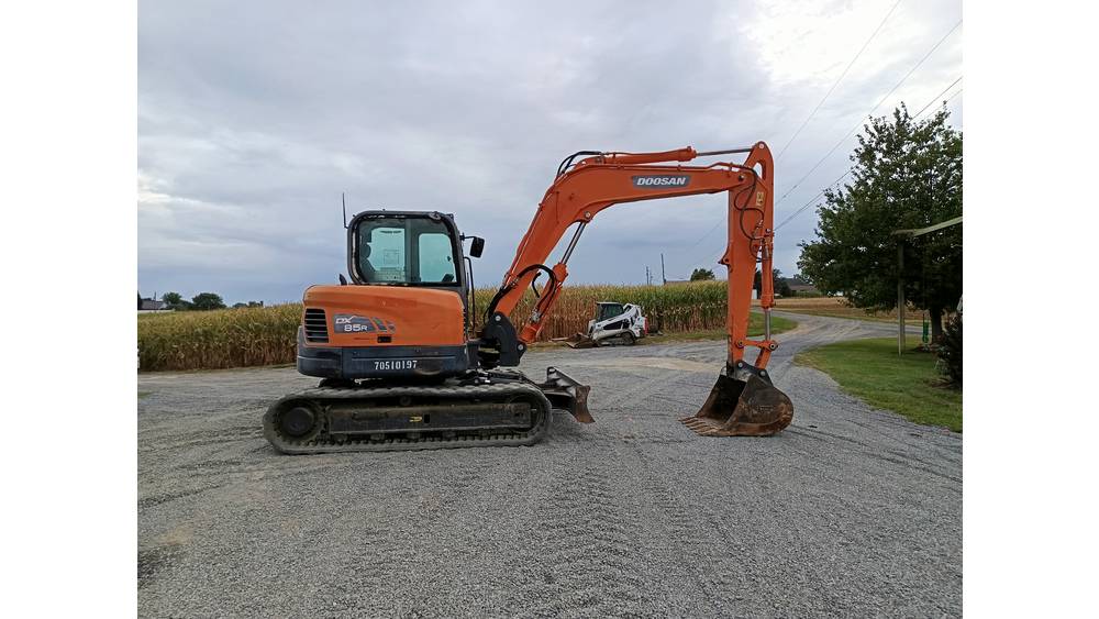 Ducati mini excavator, orange, on gravel surface with cloudy sky background.