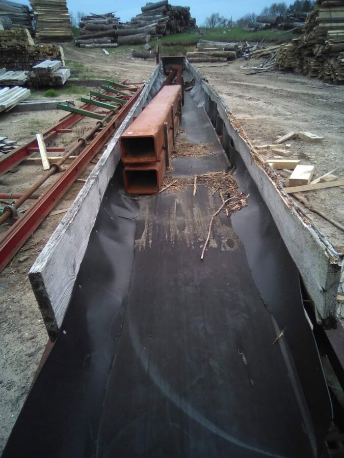 Heavy-duty metal channel with orange pipes on a construction site, surrounded by wood and metal materials.