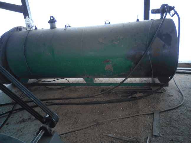 Green horizontal storage tank with valves and hoses, industrial setting, no identifiable year or model.