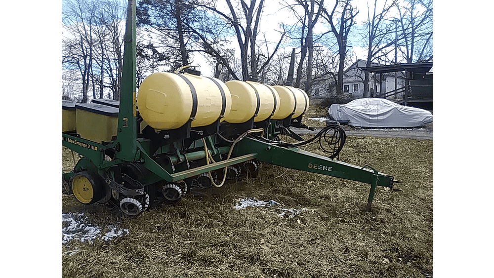 A tractor-mounted liquid fertilizer spreader with yellow tanks, green frame, and John Deere branding, set outdoors on a grass.