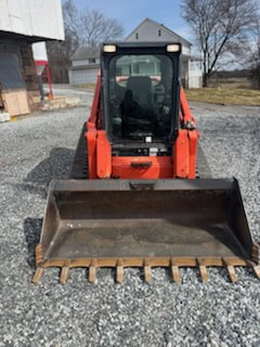 Excavator with a front bucket attachment, orange and black, parked on gravel surface outdoors.