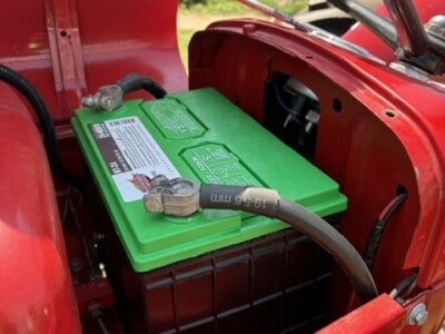 Red tractor with a large green battery and visible engine components, outdoors in a grassy area.