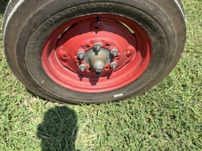 Close-up of tractor tire with red rim and black rubber tread on grassy field.