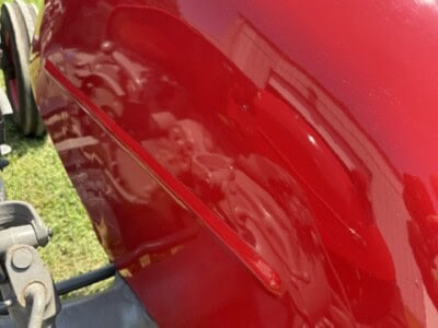 Red tractor hood with shiny finish and visible reflection of the sky and surroundings.