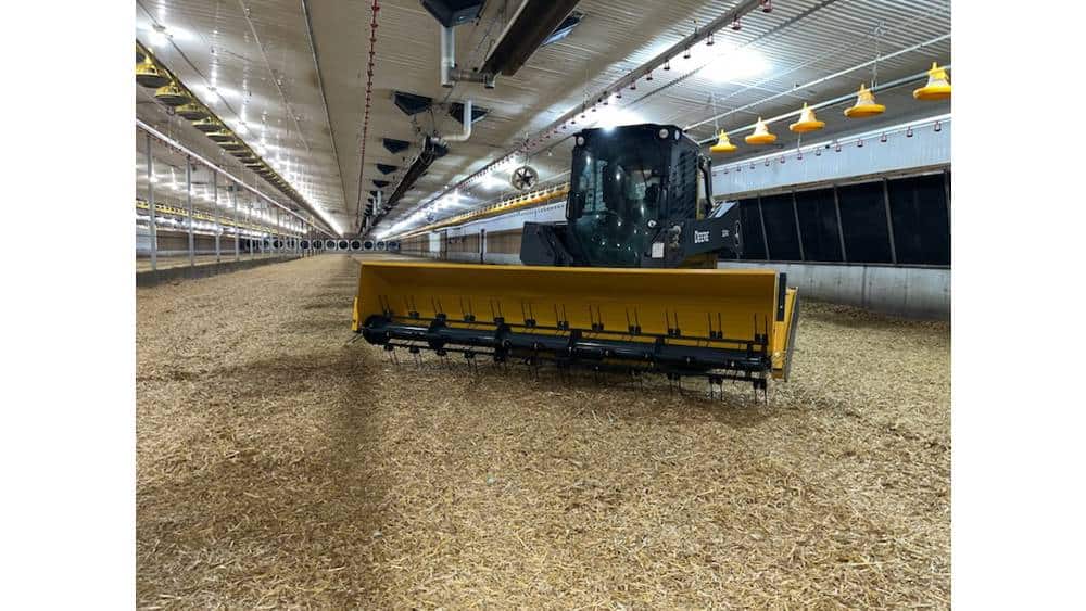 A modern indoor agricultural facility with a large yellow and black tractor equipped with a front-mounted blade.