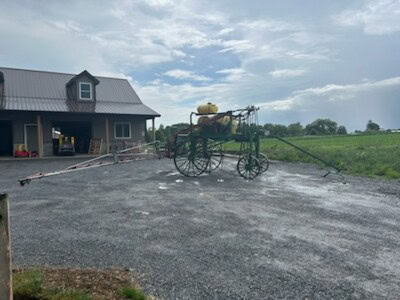 Vintage agricultural sprayer with yellow tank and large wheels on gravel driveway.