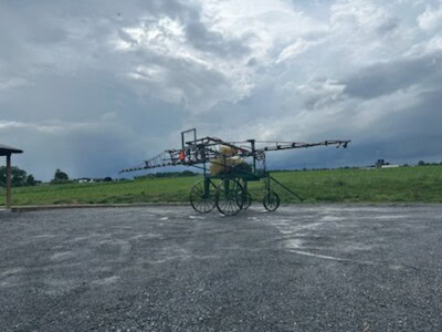 Old-fashioned tractor-mounted sprayer with long booms on a rural field under cloudy sky.