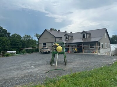 Agricultural sprayer in front of a gray house with a metal roof and multiple windows.