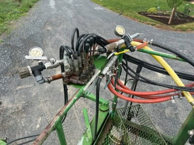 Close-up of sprayer control panel with gauges and hoses on green frame.