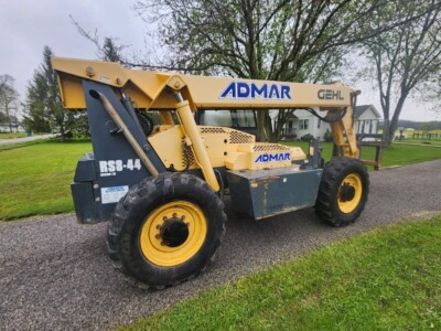 An image of a 2017 Gehl RS8-44 telehandler with yellow and black equipment, parked on a gravel path in a rural setting.