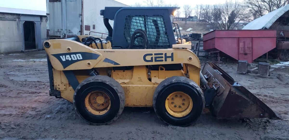 Vibrant yellow GEH V400 skid steer loader with bucket attachment, parked outdoors on a farm or construction site.