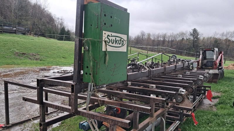 Agricultural equipment with green and black components, including a tractor and conveyor system, on a farm field in rural set.
