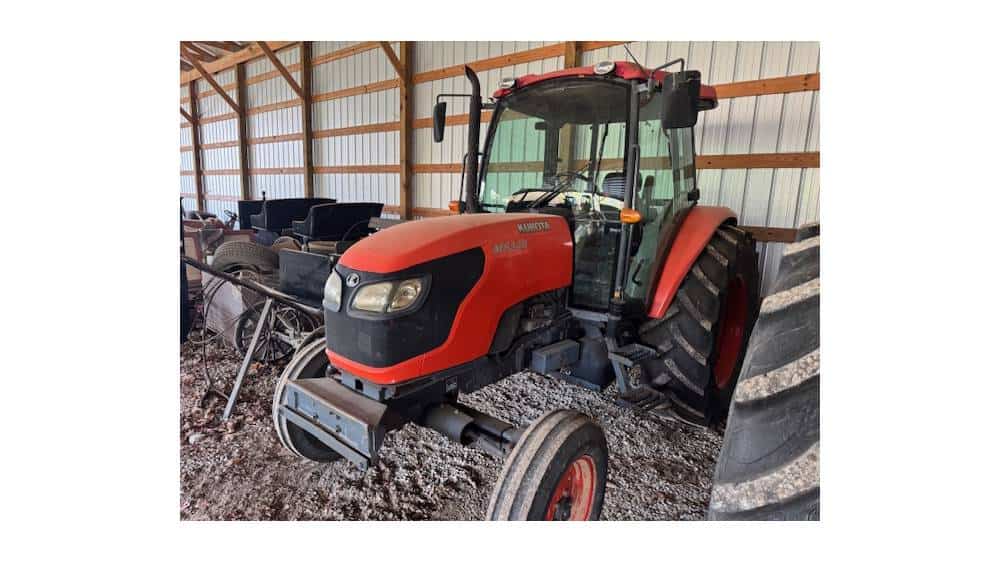 Red Mahindra tractor with enclosed cab and front loader attachment in a barn setting.