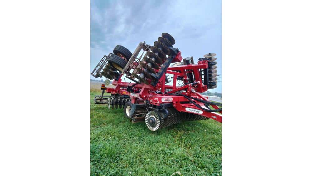 Red 2022 Case IH farm disc harrow with multiple disc blades and large tires on green field under cloudy sky.