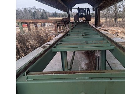 Conveyor system used for agricultural processing under a shed, with a tractor visible in the background.