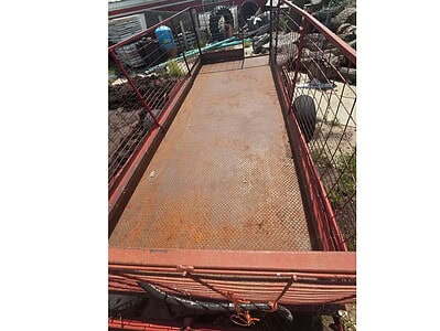 Farm equipment trailer with rusted metal bed and red frame, suitable for transporting tools and materials.