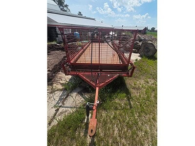 Heavy-duty red farm equipment trailer with mesh sides and wooden floor, ideal for transporting agricultural tools and materia.