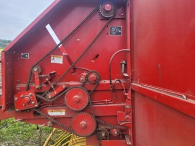 Red John Deere round baler with multiple belts and rollers, used for hay baling, outdoors on a farm.