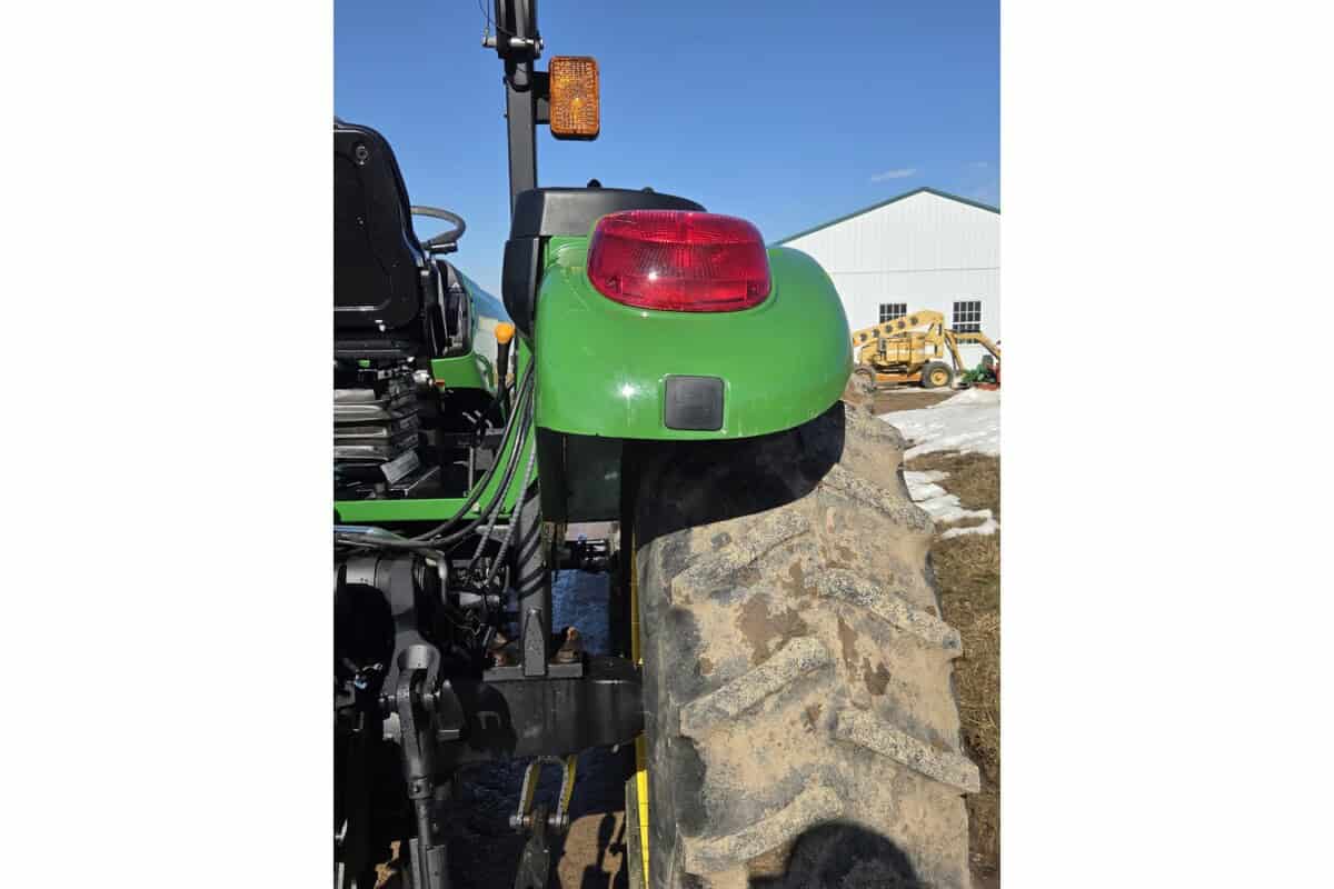 Rear view of a John Deere 5075E tractor with large rear tire and green body.