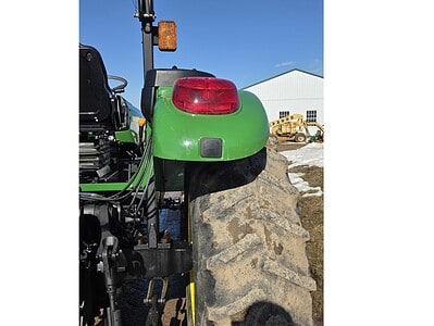 Rear view of a John Deere 5075E tractor with large rear tire and green body.