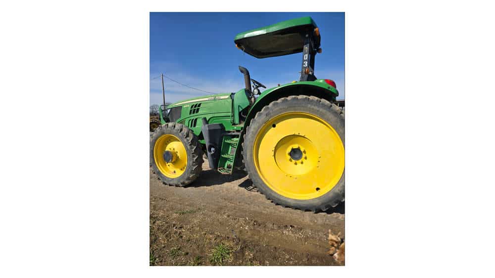 Green John Deere tractor with yellow wheels, no visible model year, on a farm field under a clear blue sky.