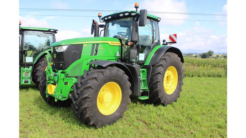 Green John Deere 8R Series tractor with large tires, parked on grassy field under blue sky.