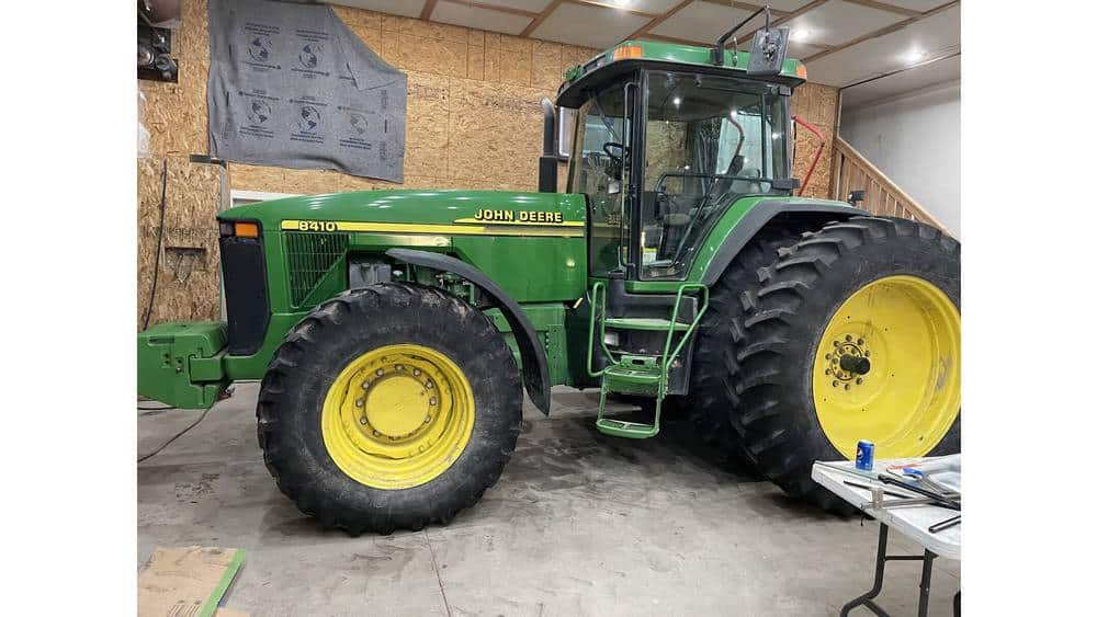 John Deere 6110 tractor, green and yellow, inside a workshop with tools and equipment.