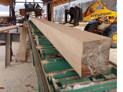 Wood beam on conveyor at sawmill, outdoor workshop with machinery and equipment.