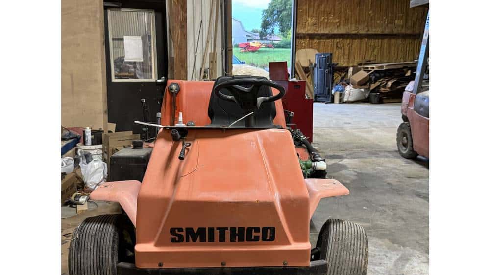 Compact orange Smithco ride-on lawn mower in a workshop setting.