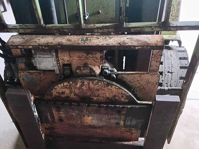 Forklift with rusted metal frame and hydraulic lift system, used for material handling.