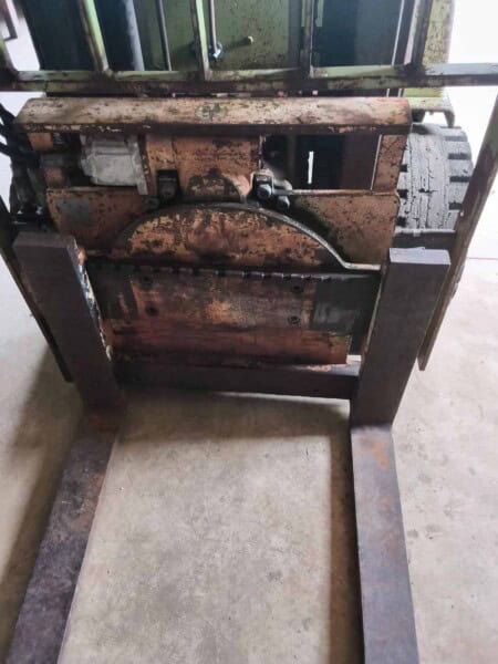 Forklift with rusted metal frame and hydraulic lift system, used for material handling.