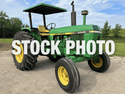 John Deere 2440 tractor, green and yellow, with canopy, parked on gravel outdoors.