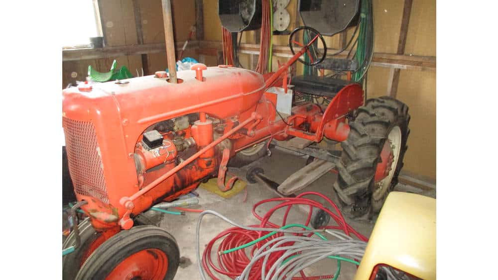 Vintage orange tractor in a barn with tools and equipment, no visible year or model.