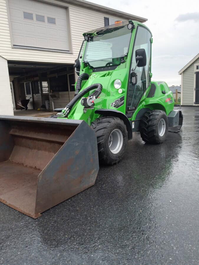 Green compact loader with front bucket, ideal for construction and landscaping projects.