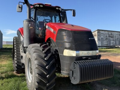 Red Case IH Magnum 340 tractor with front weight block on grassy field under blue sky.