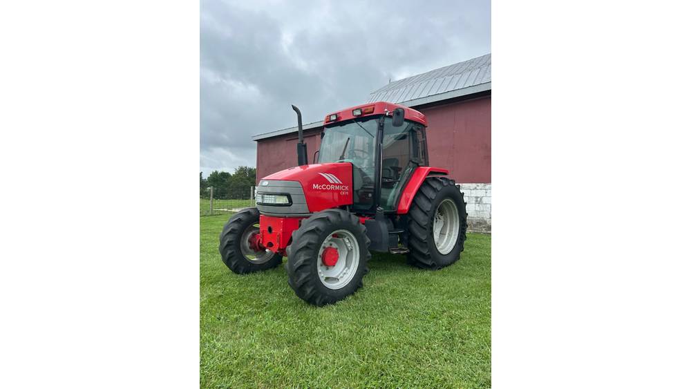 Red McCormick tractor with enclosed cab, parked on grass near a red barn under cloudy sky.