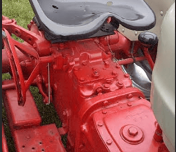 Red vintage tractor with a black seat and white body, featuring a Ford logo, parked on grass.