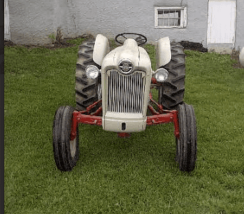 Vintage Farm Tractor, white with red chassis, front view on grass in front of a house.