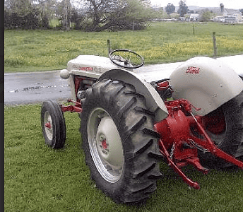 Ford 8N vintage tractor with large rear tires and steering wheel, parked on grass in a rural setting.