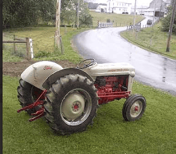Vintage Farmall tractor on a grassy field with a rural road in the background.