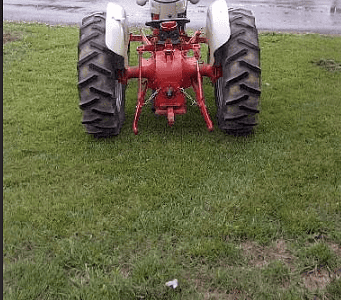 Vintage red tractor with large tires on grassy field, outdoors, overcast sky.