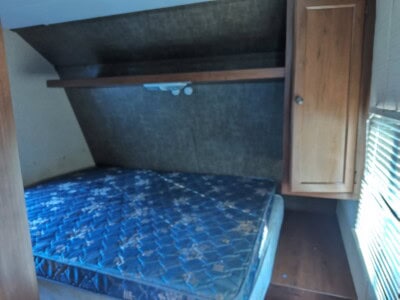 Interior view of a bedroom with a bed, wooden cabinet, and shelves, natural light from window, no specific year or model.